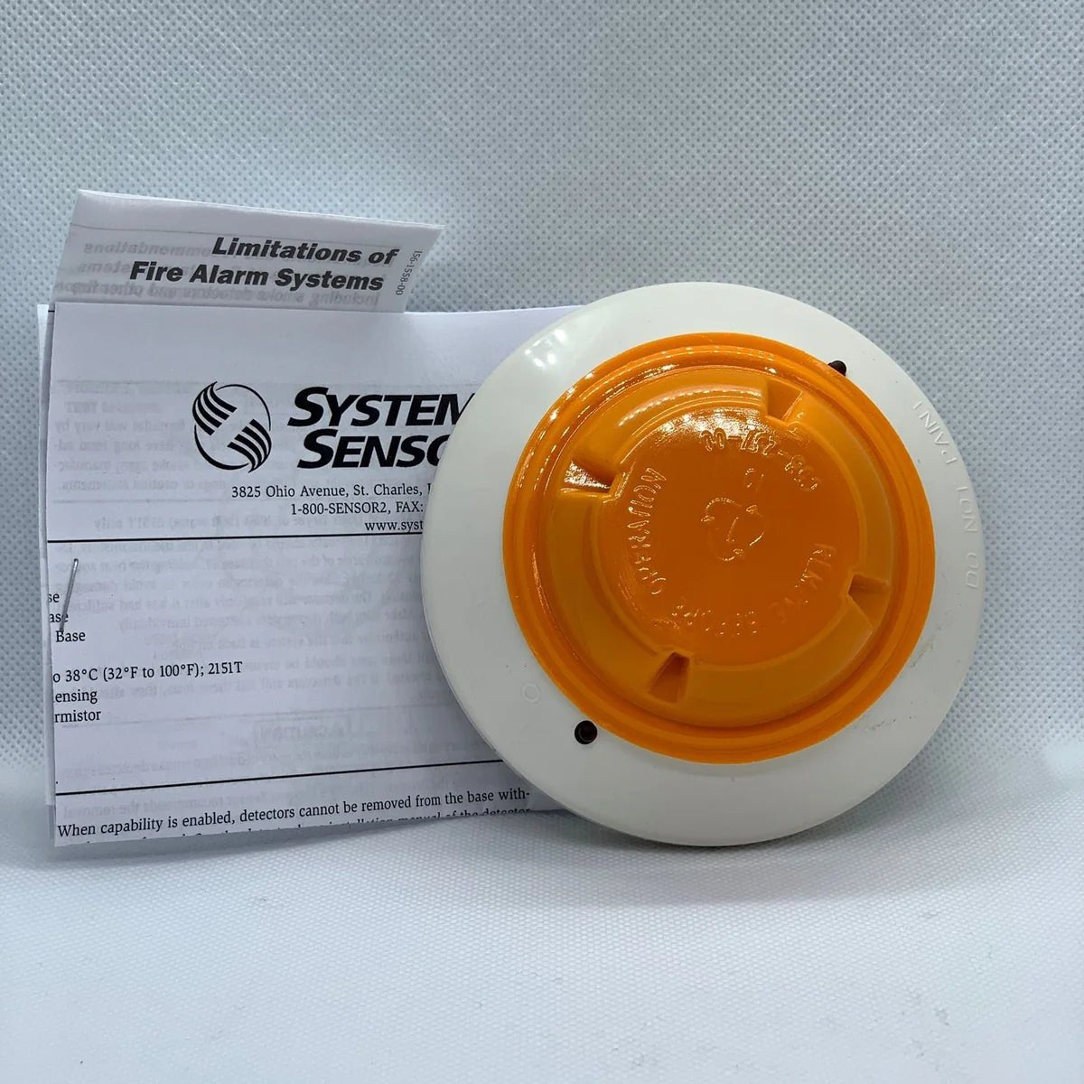 System Sensor 2151 smoke detector with alarm and testing button, mounted on a ceiling for fire safety detection.