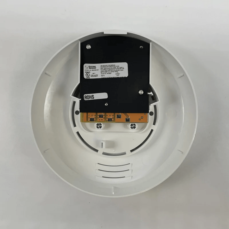 System Sensor B224RB-WH smoke detector with red LED indicator mounted on ceiling, white plastic housing, in a typical home or office setting