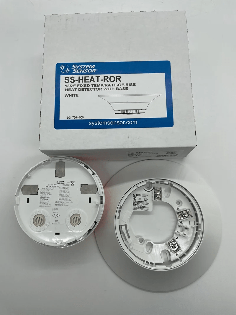 System Sensor SS-HEAT-ROR heat detector with relay output, mounted on a white wall for fire safety monitoring.