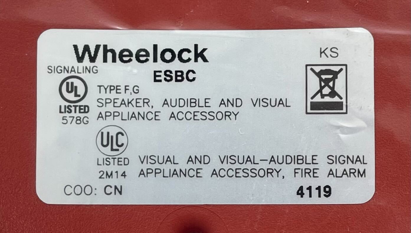 Eaton Wheelock ESBCR fire alarm with red reset switch and black housing, mounted on a wall.